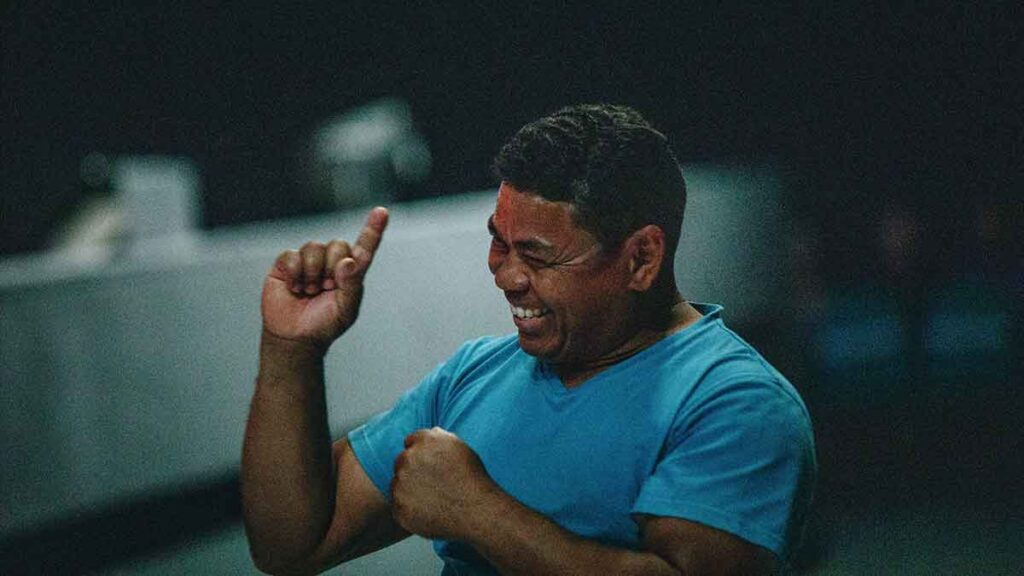 Smiling non-white man who is deaf. He's pointing his finger up.