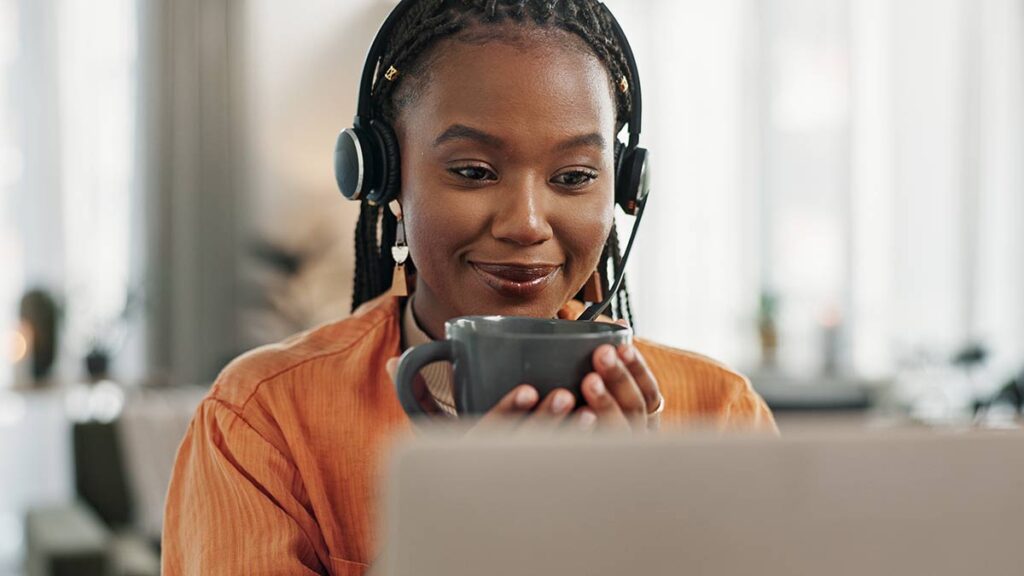 A compassionate interpreter sips coffee while studying at their laptop.