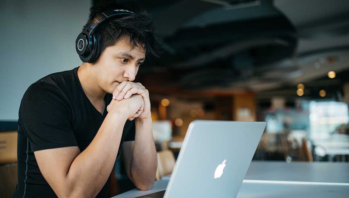 Male wearing headphones stares at his laptop while studying for his medical interpreter certification
