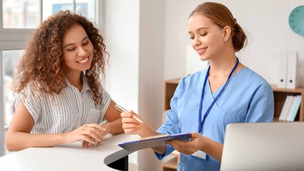 A nurse shows a medical interpreter a clipboard with the schedule of patients who need interpretation.