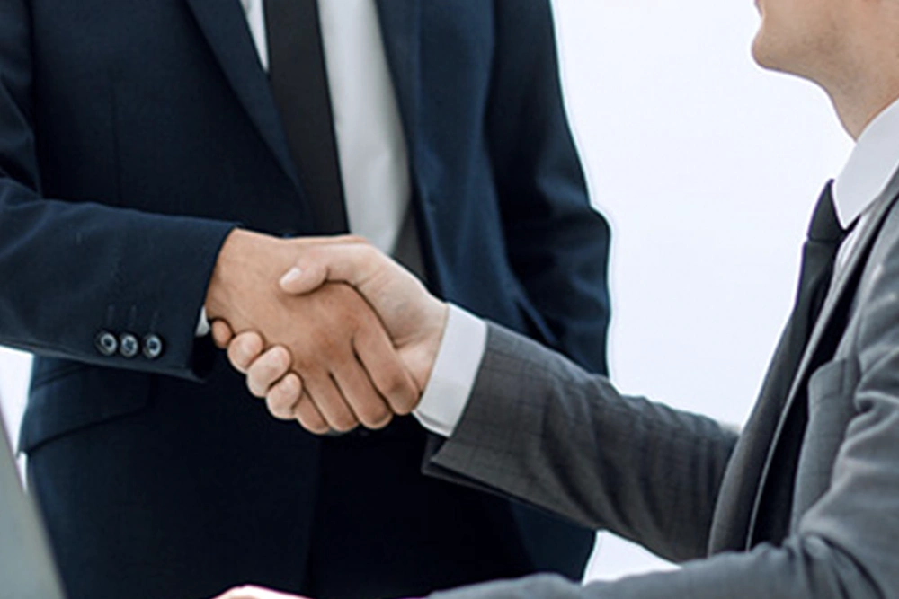 A banker and a compliance officer shake hands in an office.