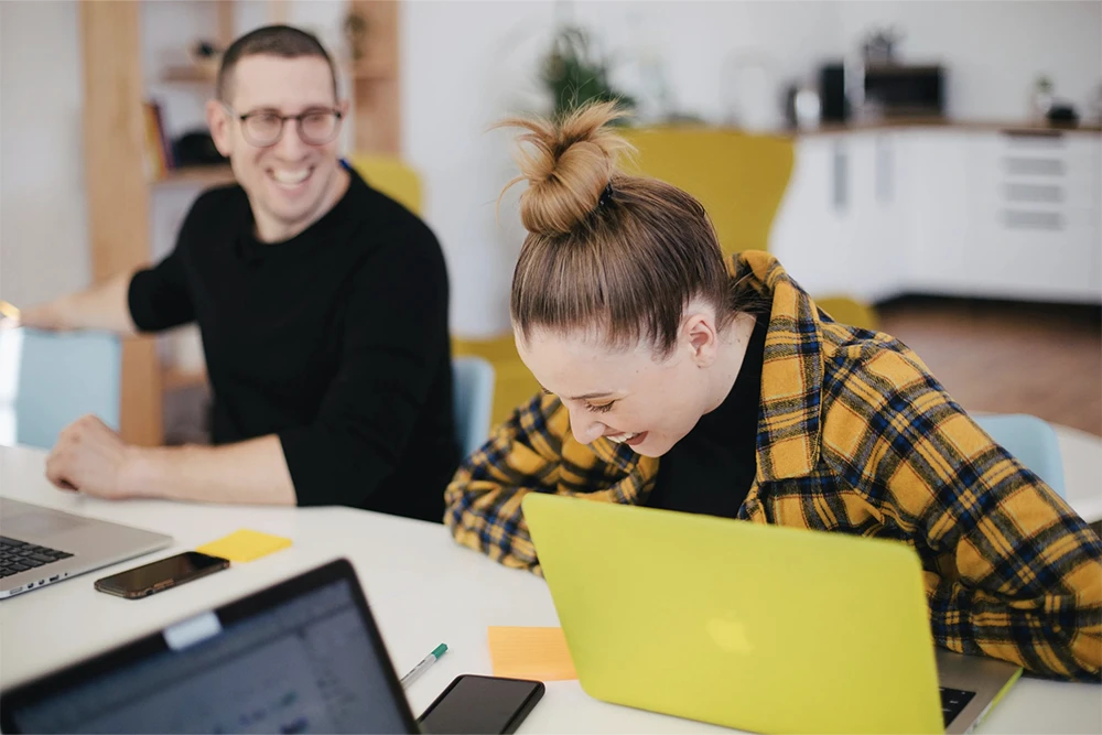 Two employees laugh together before a department meeting.
